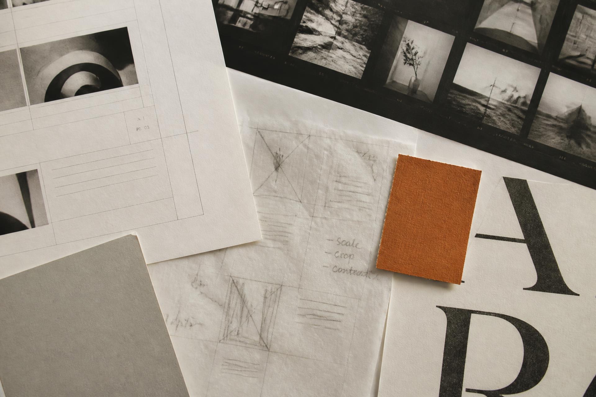 Printed layout proofs, a photographic contact sheet and paper samples arranged on a studio desk